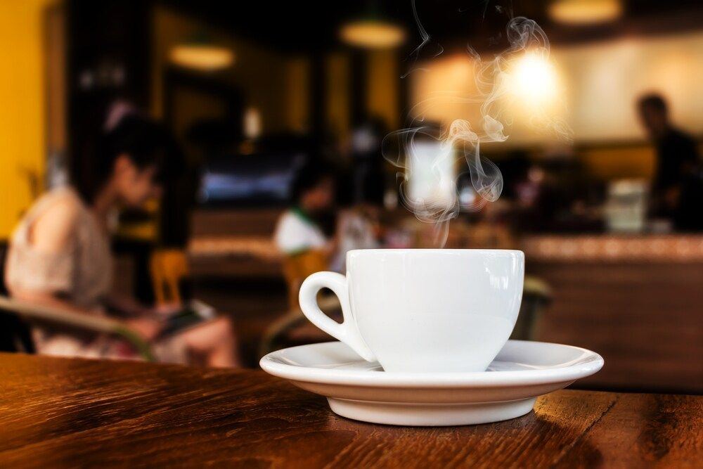 A steaming white cup of coffee on a saucer on a wooden cafe table